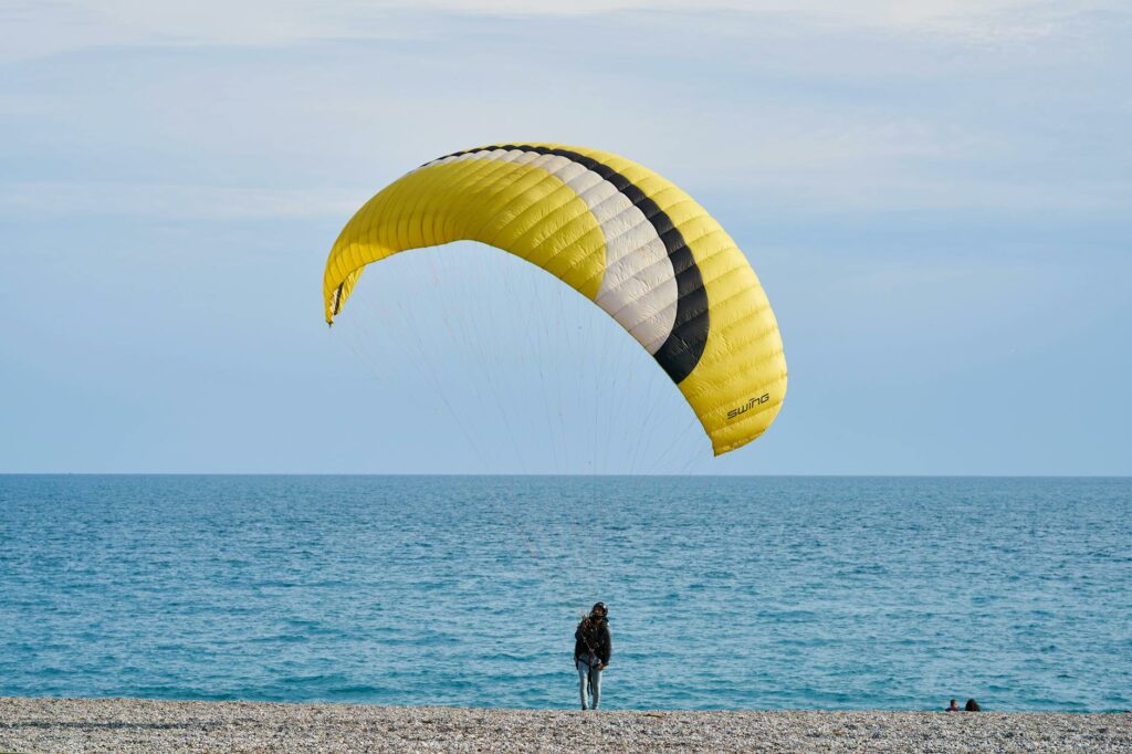 person with yellow and white gliding parachute near sea